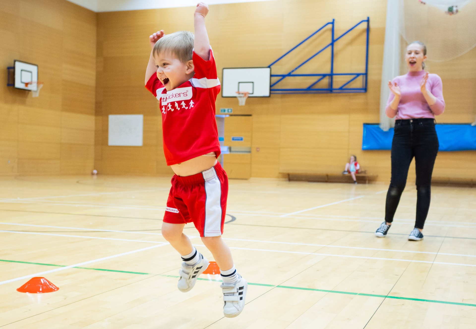 Toddler jumping with arms raised celebrating in a Little Kickers class